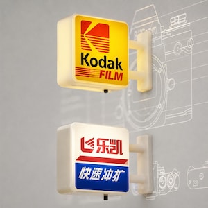 May include: Two square, wall-mounted illuminated signs. The top sign features the yellow and red Kodak Film logo. The bottom sign displays red and blue Chinese characters with a graphic icon. Both signs have white frames and mounting brackets.