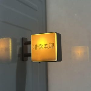 May include: A square, wall-mounted LED sign with a black frame and a glowing, warm yellow face. The sign features the Chinese characters 啡常欢迎 in black, centered on the illuminated surface, and is attached to the wall by a black bracket.
