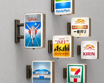 Könnte beinhalten: Eine Sammlung von sieben rechteckigen, beleuchteten Wandleuchtschildern mit verschiedenen japanischen Markenlogos wie Glico, FamilyMart, Kirin Beer, Asahi Super Dry, Lawson und 7-Eleven, die jeweils mit einer dunklen Metallhalterung befestigt sind.