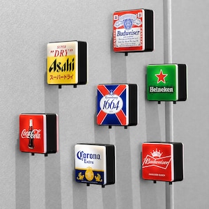 Könnte beinhalten: Eine Sammlung von sieben quadratischen, wandmontierten Leuchtschildern mit verschiedenen Getränkemarkenlogos, darunter Budweiser, Asahi Super Dry, Heineken, Kronenbourg 1664, Coca-Cola, Corona Extra und ein zweites Budweiser-Design mit Kronenlogo.