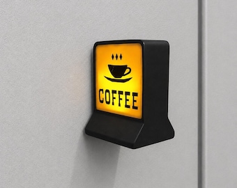 May include: A small, rectangular, black wall-mounted light fixture with a glowing yellow front panel. The panel features a black graphic of a coffee cup on a saucer with three small diamonds above it and the word COFFEE printed in black letters.