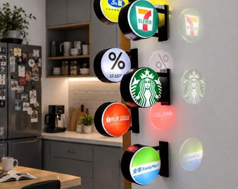 Könnte beinhalten: Ein vertikales Wanddisplay mit fünf runden, beleuchteten Schildern, die verschiedene Markenlogos wie 7-Eleven, % Arabica, Starbucks, Shopee und FamilyMart zeigen. Jedes Schild projiziert ein kreisförmiges Lichtmuster auf die weiße Wand.