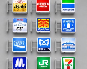 Könnte beinhalten: Eine Sammlung von zwölf quadratischen, wandmontierten Leuchtschildern mit verschiedenen japanischen Markenlogos, darunter Asahi, Yakult, FamilyMart, Meiji, Matsumoto Kiyoshi, Lawson, Pocari Sweat, Tokyo Metro, Osaka Metro, JR East und 7-Eleven.