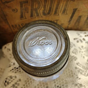 May include: Close-up of a vintage Kerr jar lid with a clear glass top and a metal band. The word "Kerr" is embossed on the glass. The lid is likely for preserving food items.