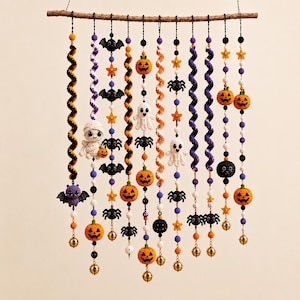 May include: A wall hanging featuring twelve vertical strands suspended from a wooden branch. The strands are decorated with crocheted Halloween figures including pumpkins, ghosts, bats, and spiders, interspersed with colorful beads and small gold bells.