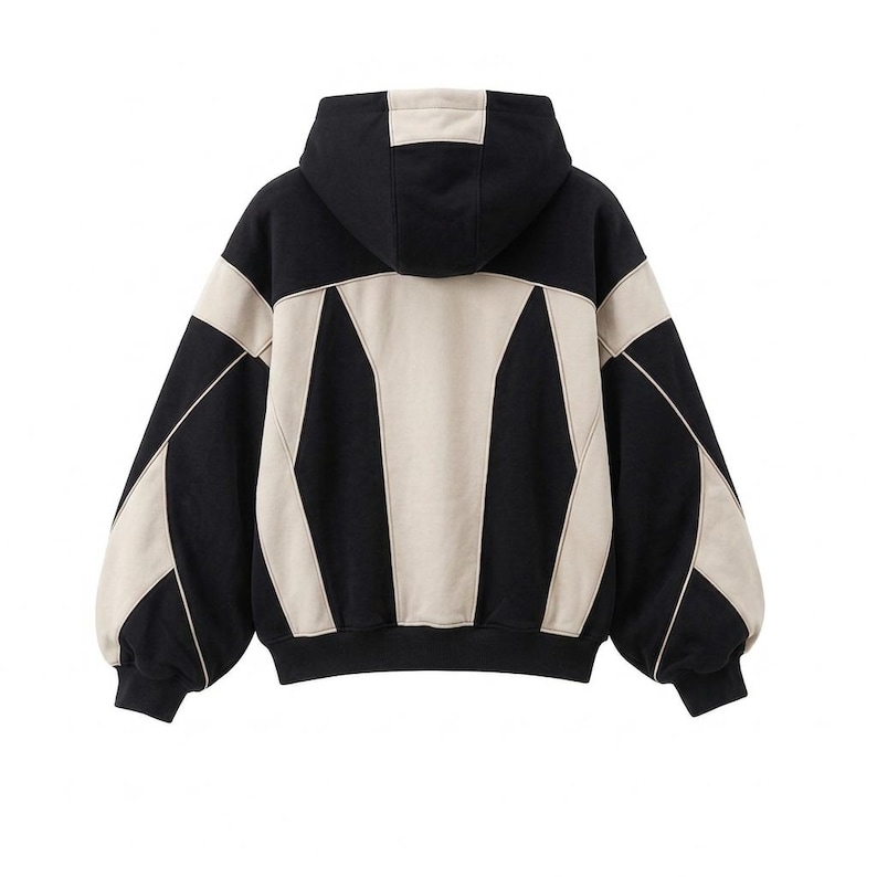 The back view of an oversized, heavyweight colorblock hoodie in black and off-white/beige, styled with retro Y2K streetwear details against a plain white background.