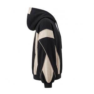 A side profile view of a black and off-white/beige heavyweight colorblock hoodie, highlighting the intricate Y2K-inspired paneling along the sleeve and torso against a clean white background.
