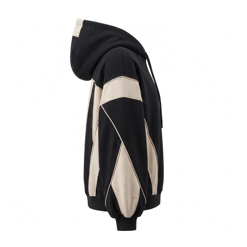 A side profile view of a black and off-white/beige heavyweight colorblock hoodie, highlighting the intricate Y2K-inspired paneling along the sleeve and torso against a clean white background.