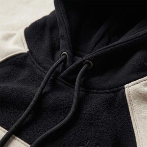 A close-up shot focused on the neckline, hood structure, and fabric texture of a heavyweight black and off-white/beige polar fleece hoodie.