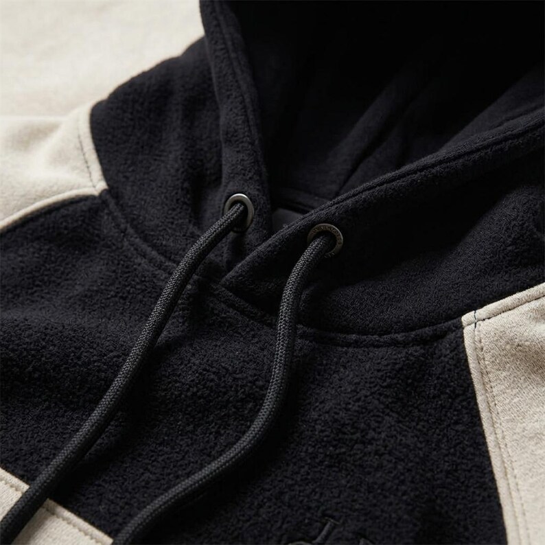A close-up shot focused on the neckline, hood structure, and fabric texture of a heavyweight black and off-white/beige polar fleece hoodie.