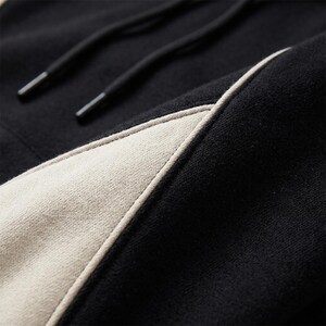A extreme close-up macro detail shot showcasing the seam work, contrast piping, and fabric texture of the black and off-white colorblock hoodie.