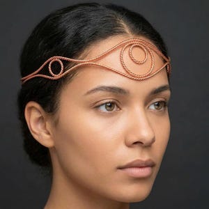 May include: A copper-colored wire headpiece worn across the forehead, featuring a twisted metal texture. The design consists of a central circular motif flanked by two smaller circular shapes, all connected by a continuous, thin, twisted wire band.