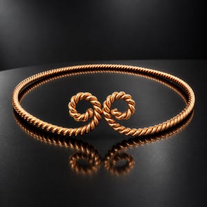 May include: A rose gold-toned metal choker necklace featuring a continuous twisted rope texture. The design consists of a circular band that terminates in two symmetrical, inward-facing spiral coils at the center front, creating an open-ended look.