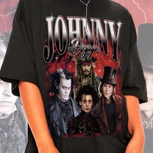 Könnte beinhalten: Ein schwarzes Kurzarm-T-Shirt mit einem Grafikdruck verschiedener Charaktere, die von Johnny Depp dargestellt werden. Der Text "JOHNNY" erscheint in einer großen metallischen Schrift über der Collage, mit "Depp" in kursiver Schrift darunter.