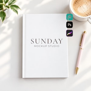 May include: A white hardcover notebook featuring the centered black text SUNDAY MOCKUP STUDIO. The notebook is positioned next to a light pink pen with gold accents, a white coffee mug filled with a brown beverage, and a small green plant.