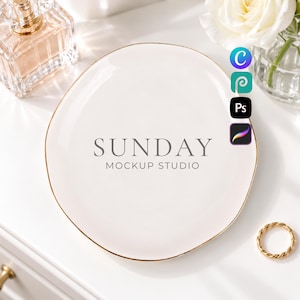May include: A round white ceramic trinket dish with a thin gold rim. The center of the dish features the grey text SUNDAY MOCKUP STUDIO. The dish is positioned on a white surface alongside a glass perfume bottle, a white rose, and a gold ring.