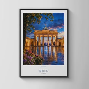 May include: A framed wall art print featuring the Brandenburg Gate in Berlin, Germany, at twilight. The illuminated monument is reflected on a wet ground, with purple flowers in the foreground and a blue and orange sunset sky above. Text reads BERLIN GERMANY.