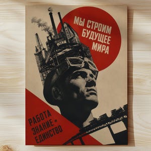 May include: A rectangular poster featuring a stylised illustration of a worker wearing goggles, with a large industrial factory structure rising from the head. The text reads "МЫ СТРОИМ БУДУЩЕЕ МИРА" and "РАБОТА ЗНАНИЕ ЕДИНСТВО" in red and black against a cream background.