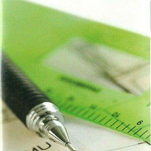 May include: A black mechanical pencil with a silver tip positioned over a green plastic ruler and a white paper surface with the text AutoSketch 10 printed at the top. The ruler features visible metric markings and numerical increments.