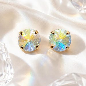 Könnte beinhalten: Ein Paar runde Ohrstecker mit irisierenden, facettierten Kristallen in goldfarbenen Metallfassungen. Die Steine zeigen ein Spektrum an lichtreflektierenden Farben, darunter Gelb, Blau und Grün, und erzeugen ein brillantes Funkeln.