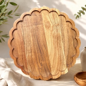Peut inclure: Un plateau de service rond en bois avec un bord festonné. Le plateau est fabriqué en bois brun clair avec un motif de grain naturel visible, présentant une surface lisse et un rebord surélevé qui suit le périmètre incurvé en forme de pétales.
