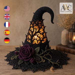 May include: A black crocheted witch hat lamp with a glowing interior, featuring a dark purple rose, green vine accents, and a small gold crescent moon charm hanging from the wide, lacy brim. The hat has a pointed, curved top and intricate lace.