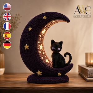 Op de afbeelding: Een donkerpaarse halve maan lamp gemaakt van gehaakt garen, met een kleine zwarte gehaakte kat met paarse ogen die op de onderste bocht zit. De maan is versierd met verschillende kleine gele gehaakte sterren en straalt een warm licht uit.