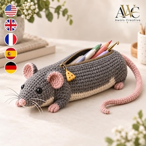 Puede incluir: Un estuche de ganchillo con forma de ratón en colores gris y crema. El ratón tiene orejas interiores rosas, nariz rosa, una larga cola rosa y ojos negros. Una cremallera dorada con un colgante amarillo en forma de queso abre el estuche.