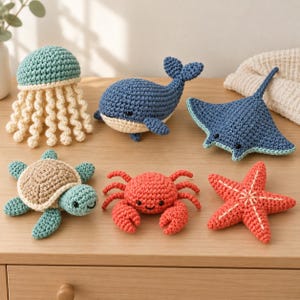 May include: A collection of six crocheted sea creatures including a teal jellyfish with cream tentacles, a blue whale, a blue stingray, a turtle with a tan shell, a red crab, and a red starfish, all featuring small black bead eyes.