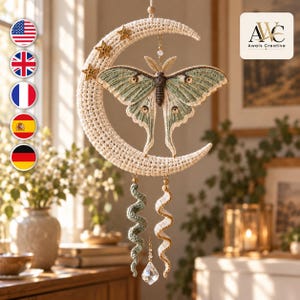 May include: A crocheted wall hanging featuring a cream-colored crescent moon adorned with three small stars and a central luna moth in shades of sage green and cream. Two spiraling yarn tassels hang below, accented by a clear faceted crystal pendant.
