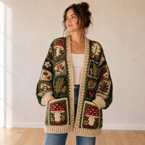 May include: A long-sleeved crochet cardigan featuring a patchwork design of forest-themed motifs including red and white mushrooms, brown oak leaves, a snail, and a moth. The garment has a cream-colored border, ribbed cuffs, and two front pockets.