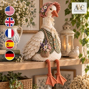May include: A crocheted goose figurine wearing a pink floral bonnet, a green vest with three buttons, and a small basket filled with flowers. The goose has a white body, orange beak, and orange webbed feet, with the text Awais Creative visible.