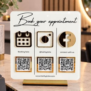 Könnte beinhalten: Ein weißes, quadratisches Acrylschild mit goldenen Akzenten und der Aufschrift Book your appointment. Es zeigt drei Symbole für Kalender, Instagram und Facebook, jeweils mit einem QR-Code und Beschriftungen wie Booking here, @hairbyitshe, connect with us sowie der Website www.hairbyitshe.com.