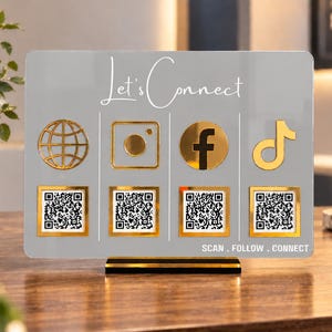 May include: A rectangular grey acrylic sign with a gold base featuring the white text Let's Connect at the top and SCAN . FOLLOW . CONNECT at the bottom. It displays four gold social media icons above four square QR codes with gold borders.