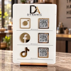 May include: A white rectangular acrylic sign with a gold base featuring the Dynamic Acrylic logo at the top. It displays three social media icons in gold, each paired with a corresponding QR code and the handle @dynamicacrylic below.