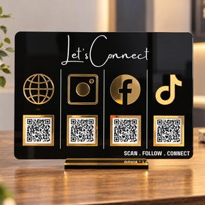 May include: A rectangular black acrylic sign with gold accents featuring the text Let's Connect at the top and SCAN . FOLLOW . CONNECT at the bottom. It displays four gold social media icons above four individual white QR code squares.