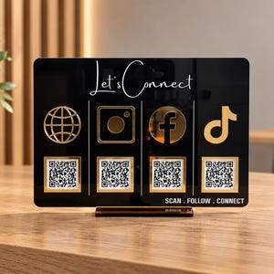 May include: A rectangular black acrylic sign with gold accents featuring the text Let's Connect at the top and SCAN . FOLLOW . CONNECT at the bottom. It displays four gold social media icons above four individual square QR code stickers.