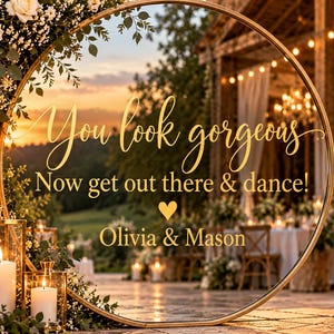 May include: A large circular gold-framed mirror featuring the gold text "You look gorgeous, Now get out there & dance!" with a heart symbol and the names "Olivia & Mason" printed in the centre, positioned outdoors at a wedding reception.