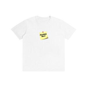May include: A white short-sleeved t-shirt featuring a graphic of a yellow square sticky note pinned to the center of the chest. The sticky note has the text GOOBER BOIS written in black ink and is secured with a small red push pin at the top.
