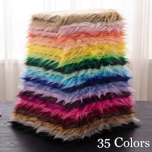 Peut inclure: Une pile de carrés de tissu en fausse fourrure dans une grande variété de couleurs, notamment beige, rose, orange, jaune, vert, bleu, violet, magenta, marron et noir. Le texte 35 Colors est imprimé en blanc dans le coin inférieur droit.