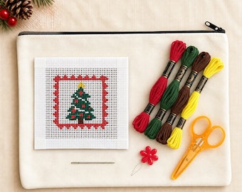 Puede incluir: Un kit de punto de aguja que incluye un lienzo cuadrado con un diseño de árbol de Navidad bordado, cuatro madejas de hilo de bordar en rojo, verde, marrón y amarillo, una aguja de metal, un enhebrador de flores rojo y tijeras naranjas.