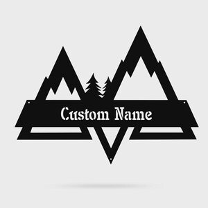 May include: A black metal wall sign featuring a mountain range silhouette with two pine trees in the center. A horizontal banner across the middle contains the text Custom Name in a white stencil-style font. The design has geometric triangular shapes.