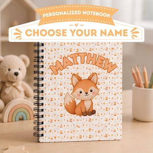 Puede incluir: Un cuaderno de espiral con un patrón repetitivo de pequeños zorros naranjas y estrellas sobre un fondo blanco. El nombre MATTHEW está impreso en letras grandes de color naranja sobre una ilustración central de un zorro sentado. Una pancarta dice PERSONALIZED NOTEBOOK CHOOSE YOUR NAME.