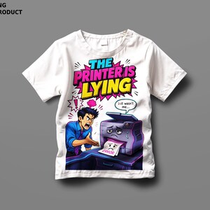 May include: A white t-shirt featuring a comic-style graphic of an angry person gesturing toward a sad printer. The text reads THE PRINTER IS LYING, with a speech bubble from the printer saying i-it wasn't me and a paper sheet labeled ERROR.