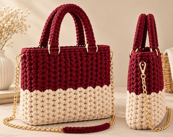 Può includere: Una borsa a mano bicolore realizzata in filato spesso color bordeaux scuro e crema. La borsa presenta due robusti manici all'uncinetto, finiture in metallo dorato e una tracolla a catena dorata abbinata con una spallina in filato bordeaux.