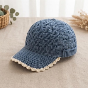 Pu&ograve; includere: Un berretto da baseball blu realizzato con un motivo a uncinetto a intreccio testurizzato. Il berretto presenta una corona strutturata e una visiera curva rifinita con un bordo decorativo smerlato color crema lungo tutto il perimetro esterno.