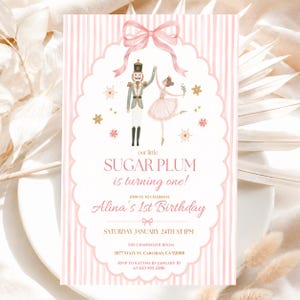 May include: A rectangular birthday invitation card with a pink and white striped background. It features a watercolor illustration of a nutcracker and a ballerina under a pink bow. Text reads: our little SUGAR PLUM is turning one! Alina's 1st Birthday.