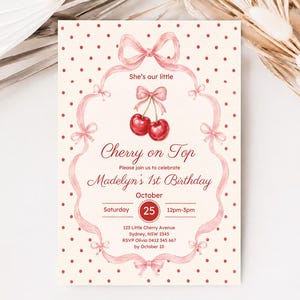 Op de afbeelding: Een verjaardagsuitnodigingskaart met een crèmekleurige achtergrond met rode stippen, een roze lintrand en een aquarelillustratie van twee kersen met een strik. De tekst bevat She's our little Cherry on Top, Madelyn's 1st Birthday, October 25.