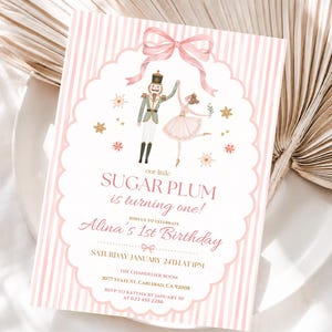 Op de afbeelding: Een rechthoekige verjaardagsuitnodiging met een roze en wit gestreepte rand. Het midden bevat een geschulpt wit kader met een roze strik, een notenkraker en een ballerina. De tekst luidt: our little SUGAR PLUM is turning one! Alina's 1st Birthday, Saturday January 24th at 1pm, The Chandelier Room, 3077 State St, Carlsbad, CA 92008, RSVP to Katyna by January 10 at 623 455-2286.