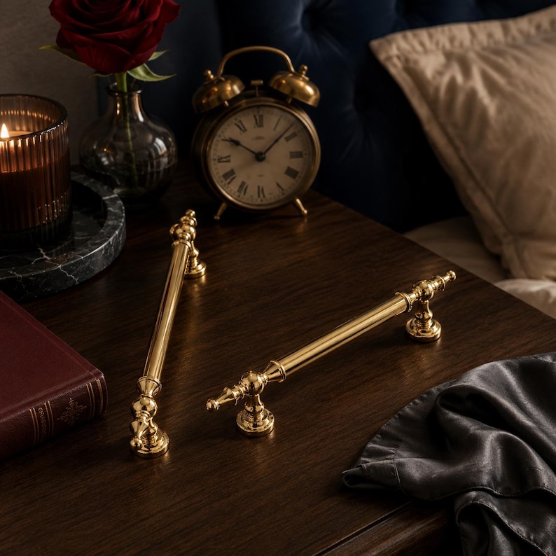 May include: Two polished gold-tone metal cabinet pulls with a cylindrical bar design and decorative finials at each end. The hardware features a smooth, reflective finish and circular mounting bases, presented as a pair of matching furniture handles.